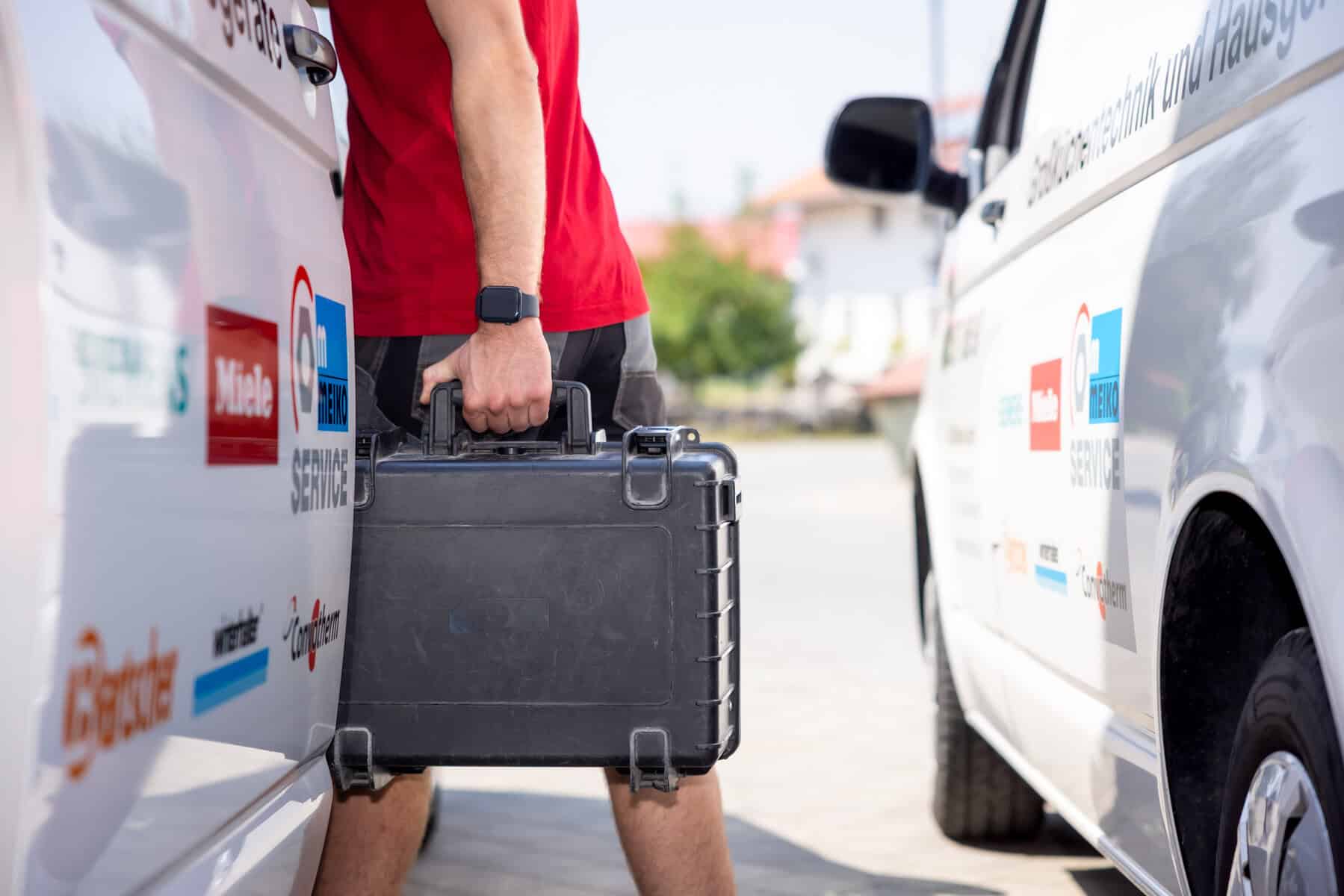 Elektriker trägt Werkzeugkoffer zwischen Firmenfahrzeugen.