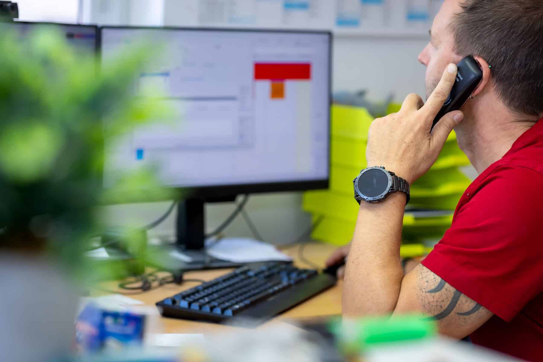 Elektriker bei der Arbeit im Büro, telefoniert und arbeitet am Computer.