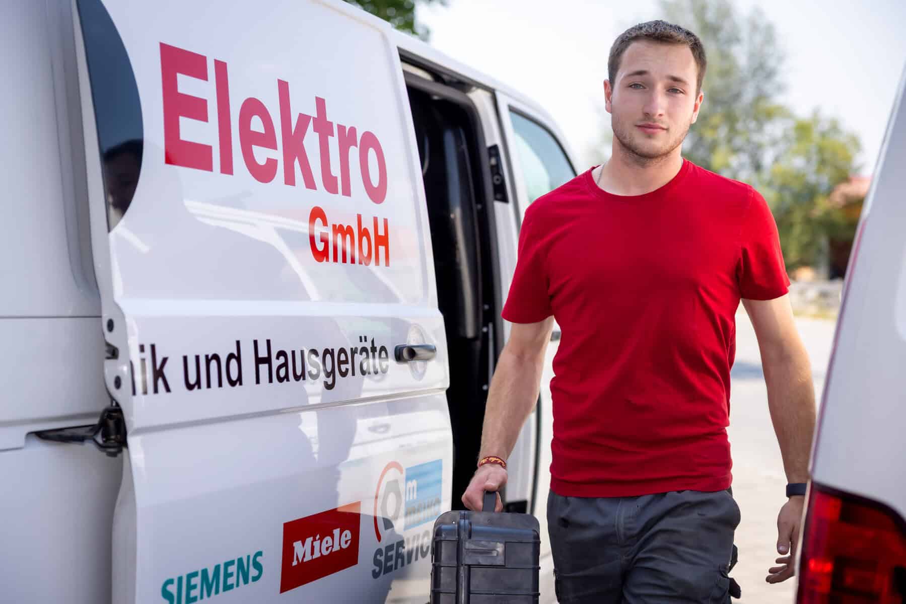 Elektriker bei K&R Elektro GmbH mit Werkzeugkoffer vor Einsatzfahrzeug.