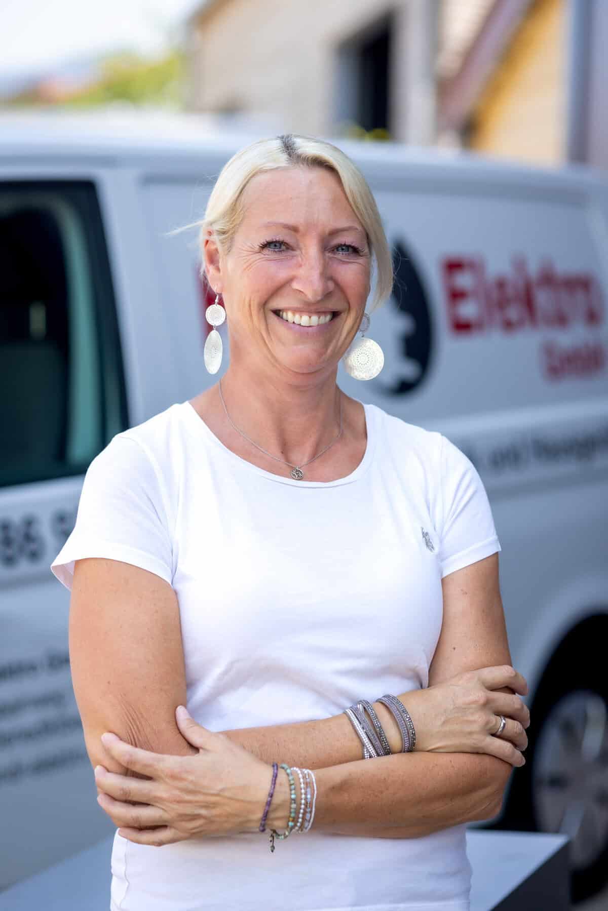 Lächelnde Elektrikerin vor Firmenfahrzeug von K&R Elektro GmbH.
