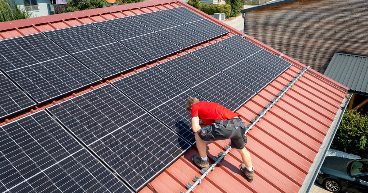 Techniker installiert Solarpanels auf einem roten Dach.